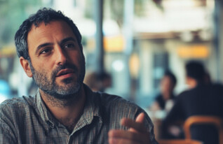 גבר יושב בבית קפה ומדבר (AI: mako)