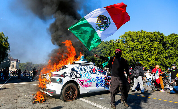 מפגין עם רכב שרוף של Waymo (צילום: BENJAMIN HANSON/Middle East Images/AFP via Getty Images)
