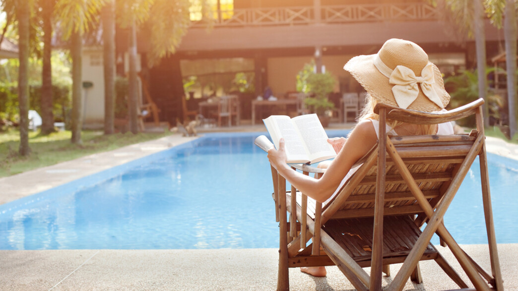 אישה יושבת מול בריכה וקוראת ספר