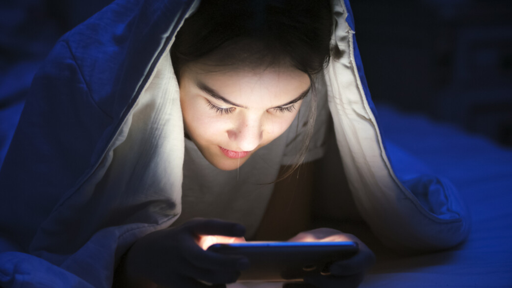 ילדה מתחת לשמיכה עם טלפון סלולרי