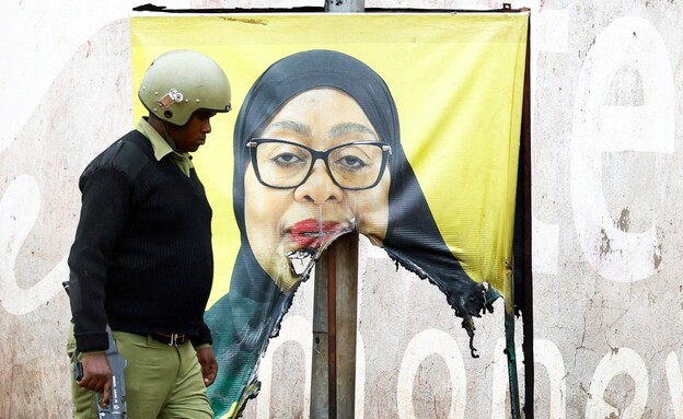 שוטר טנזני ליד שלט מושחת של הנשיאה חסן