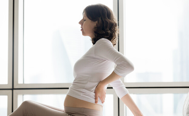 אישה בהיריון יושבת על מיטה ומחזיקה את הגב