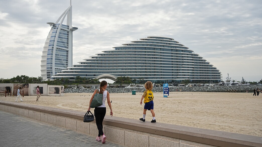 אישה וילדה צועדים לאורך חוף הים בדובאי, כשברקע מלונות 