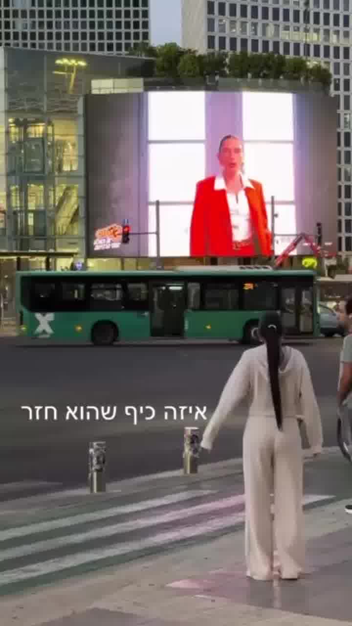 עומר לוי חוגגת מול הפרסומת שלה שמאירה את כל צומת עזריאלי