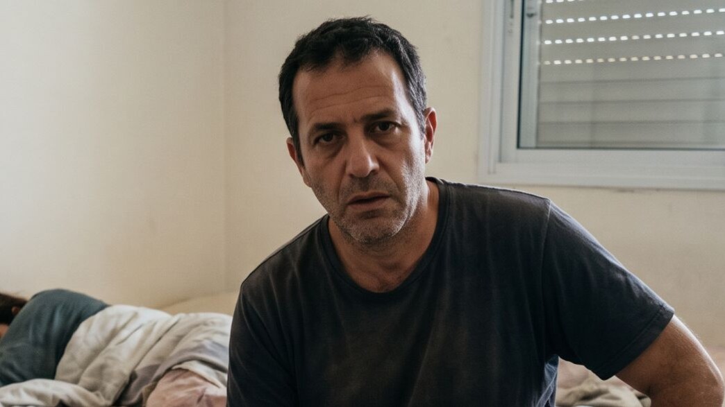 גבר יושב על מיטה עם אישה ברקע גבר יושב על מיטה עם אישה ברקע